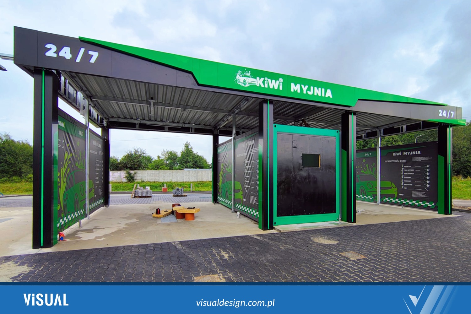 Nowoczesna, samoobsługowa myjnia samochodowa Kiwi z czarno-zieloną konstrukcją, prezentująca logo firmy i instrukcje użytkowania. Widok z zewnątrz, w dzień.
