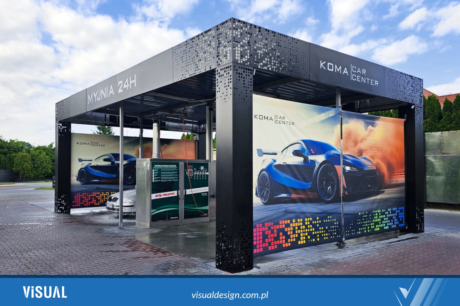 Nowoczesna konstrukcja myjni samochodowej KOMA CAR CENTER z perforowanymi elementami i reklamami aut. Widoczny automat myjący i zaparkowany samochód.