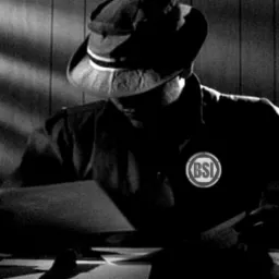 Czarno-białe zdjęcie mężczyzny w kapeluszu, pochylonego nad dokumentami na biurku, z odznaką BSI na ubraniu.