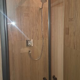 Arkadiusz Wroński Instalacje i Remonty - Nowoczesna kabina prysznicowa z deszczownicą i panelami ściennymi imitującymi drewno. Minimalistyczny design, stonowana kolorystyka, oświetlenie LED.
