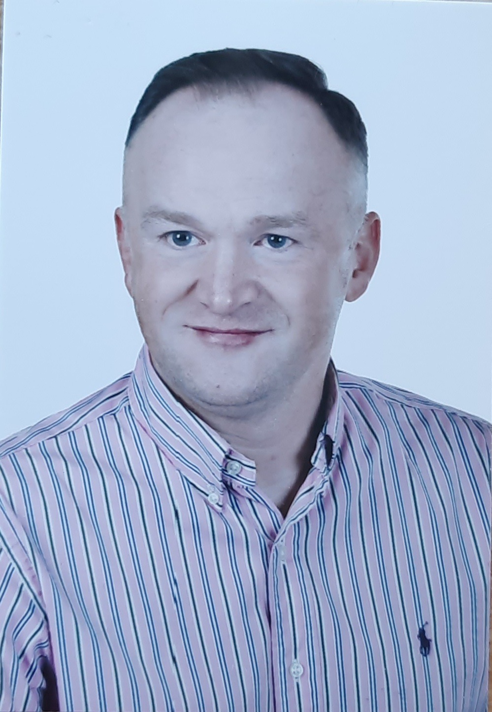 Portret mężczyzny w różowo-białej koszuli w paski z logo Polo Ralph Lauren, uśmiechniętego na białym tle.