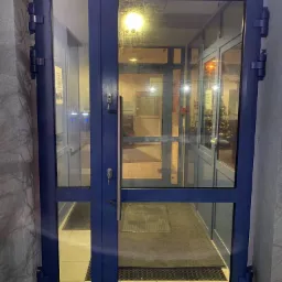 Niebieskie, przeszklone drzwi wejściowe z widocznym wnętrzem budynku, w tle choinka świąteczna.