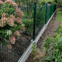 Zielone ogrodzenie panelowe z podmurówką betonową w ogrodzie z hortensjami i drzewami.