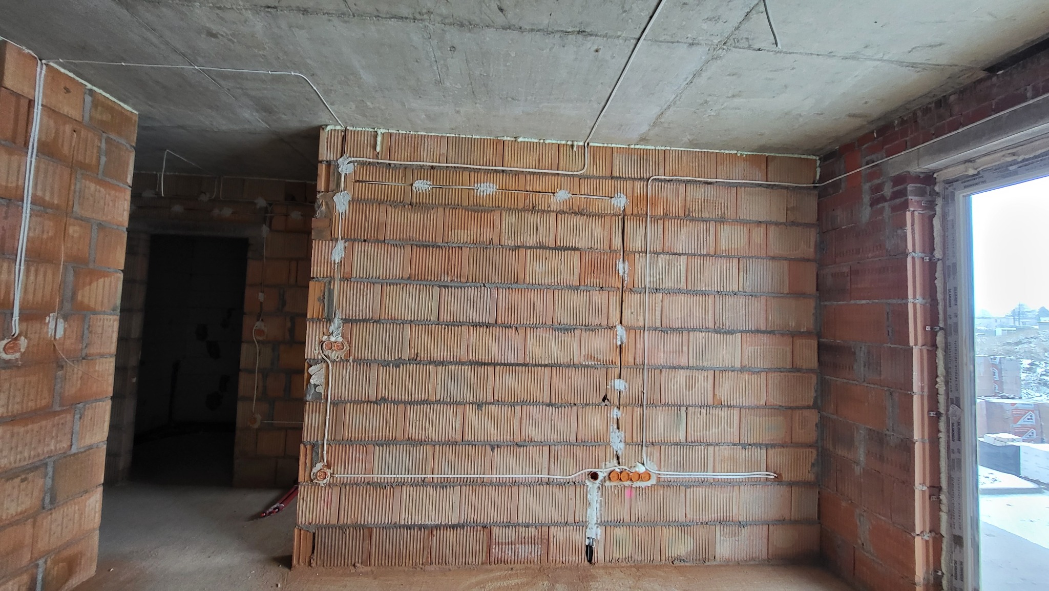Surowy mur z pustaków ceramicznych w trakcie montażu instalacji elektrycznej, widoczne kable i puszki zabezpieczone gipsem, stan deweloperski.
