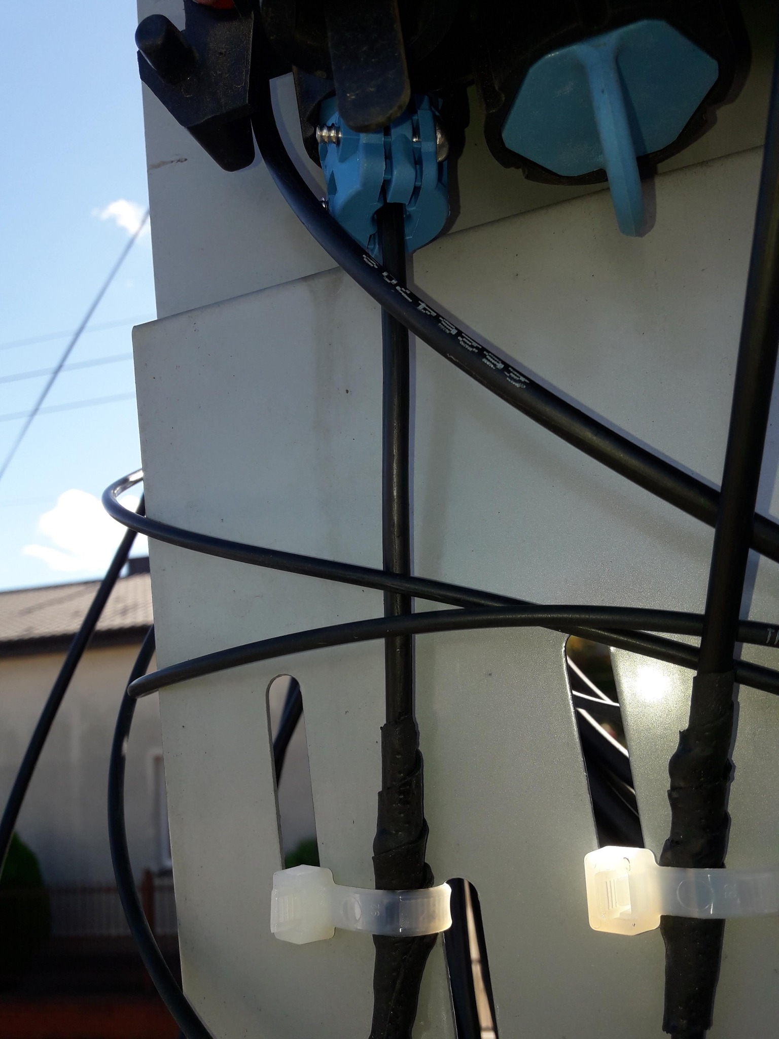 Szczegółowe ujęcie kabli telekomunikacyjnych przymocowanych do skrzynki przyłączeniowej na zewnątrz budynku, zabezpieczonych plastikowymi opaskami zaciskowymi oraz owiniętych taśmą izolacyjną.