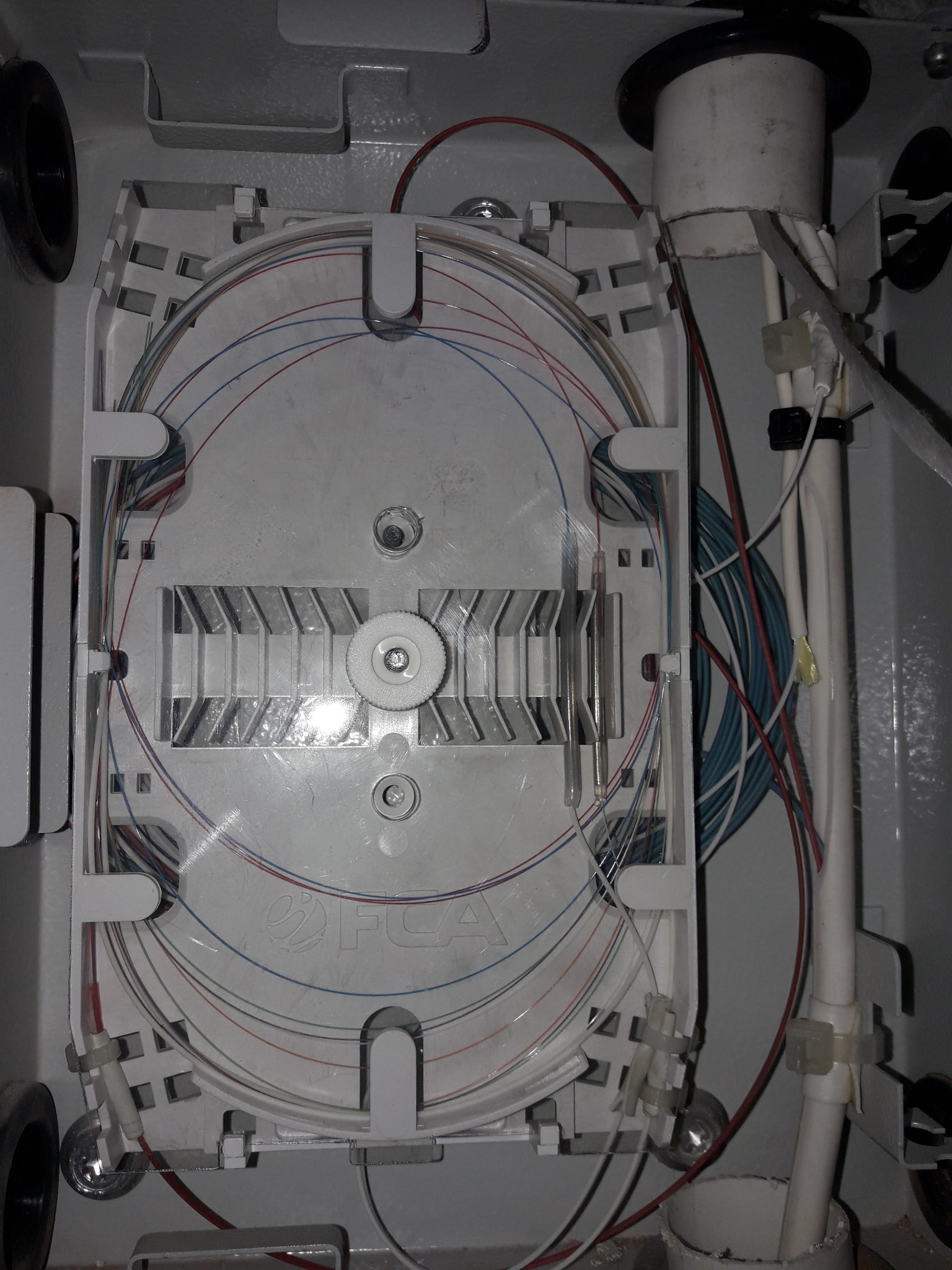 Rozdzielnica światłowodowa z ułożonymi kablami wewnątrz obudowy, widoczne kable w różnych kolorach oraz elementy mocujące.