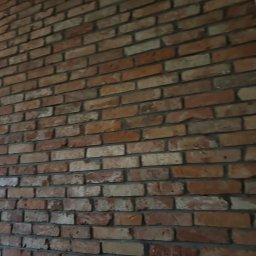 Piotr Baniewicz - Ściana z cegły klinkierowej w odcieniach czerwieni i brązu, z wyraźną fakturą i fugami. Widoczne nierówności i naturalne przebarwienia cegieł.