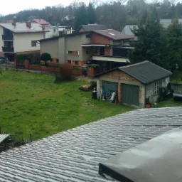 Szary dach z blachy falistej widziany z góry, w tle zabudowa jednorodzinna i zieleń trawnika.