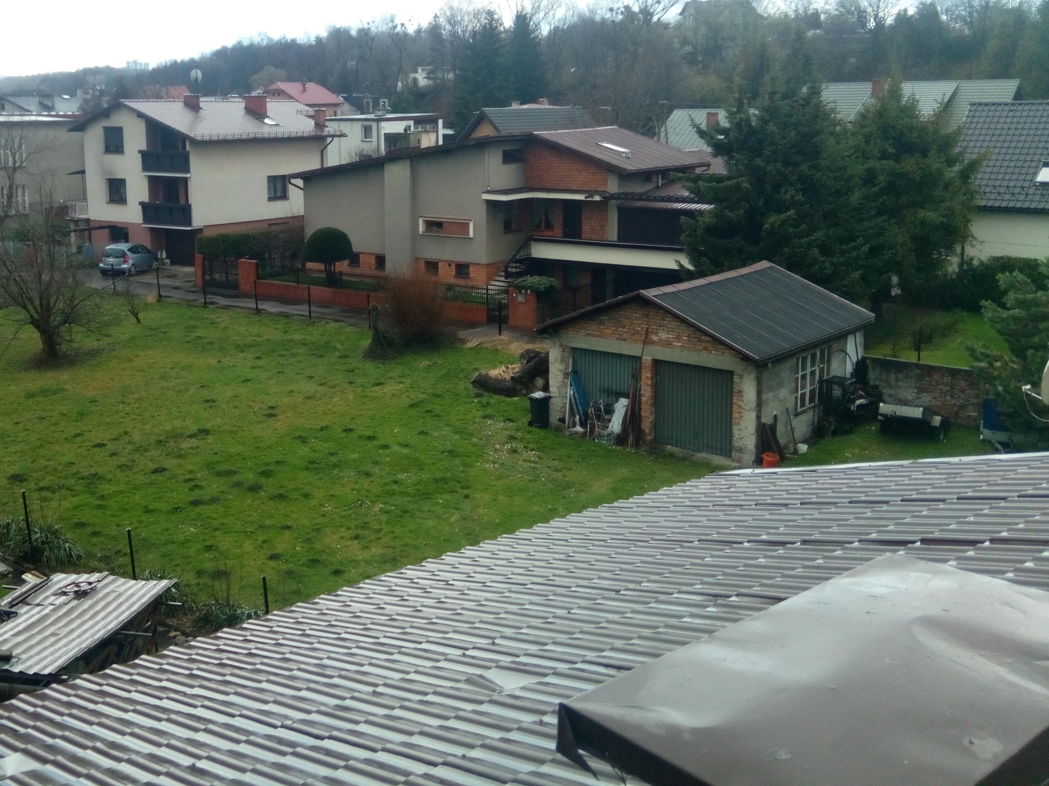 Szary dach z blachy falistej widziany z góry, w tle zabudowa jednorodzinna i zieleń trawnika.