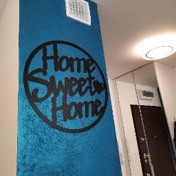 Garant-BUD - Błękitna ściana z dekoracyjną strukturą i czarnym napisem 'Home Sweet Home', wentylacja w górnej części ściany, widoczny fragment przedpokoju z drzwiami.