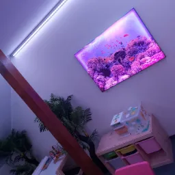 Pokój dziecięcy z podświetleniem LED i telewizorem imitującym akwarium z rybami, drewniana belka konstrukcyjna, stolik z krzesełkami i regał z pojemnikami na zabawki.