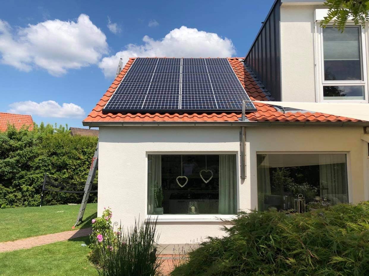 Panele słoneczne na pomarańczowym dachu domu jednorodzinnego z drabiną opartą o ścianę, widok z ogrodu w słoneczny dzień.