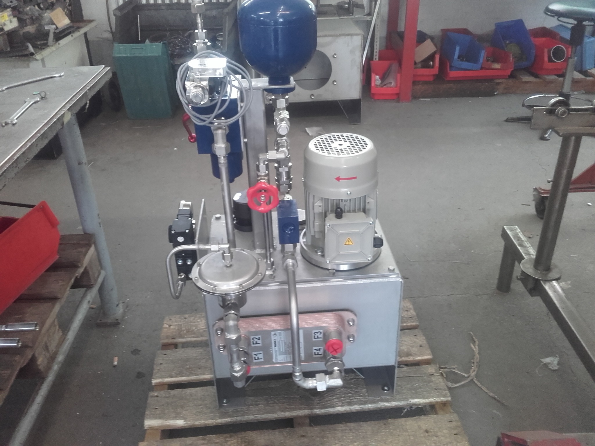 Kompletna, zmontowana przemysłowa instalacja hydrauliczna na palecie, z widocznymi elementami: zbiornik ciśnieniowy, silnik elektryczny, wymiennik ciepła płytowy z oznaczeniami F1-F4, zawory kulowe...