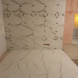 Ściana i podłoga w trakcie układania płytek imitujących marmur, z użyciem klipsów poziomujących, widoczne gniazdka elektryczne.