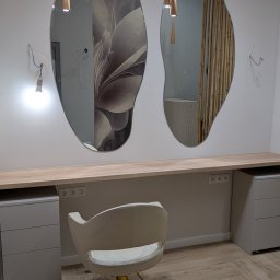 DREAMWOOD SYSTEM Przemysław Pachuta - Dwa asymetryczne lustra na ścianie nad blatem z szafkami, kremowe krzesło obrotowe z złotą podstawą na parkiecie ułożonym w jodełkę, wiszące lampy z drewnianymi kloszami, widoczne niedokończone...