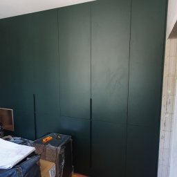 DREAMWOOD SYSTEM Przemysław Pachuta - Ciemnozielona szafa wnękowa z długimi, pionowymi uchwytami, widoczna w trakcie montażu; podłoga zabezpieczona folią budowlaną, obok pralka i narzędzia.