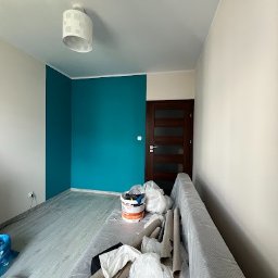 AROU Home Arkadiusz Nejman - Świeżo pomalowany pokój z turkusową ścianą, zabezpieczona folią kanapa, puszki z farbą i wałki malarskie na podłodze.