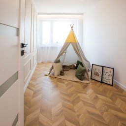 AROU Home Arkadiusz Nejman - Jasne wnętrze pokoju dziecięcego z parkietem w jodełkę, tipi i dekoracjami ściennymi. Widoczne drzwi z nowoczesnym designem i subtelne oświetlenie.
