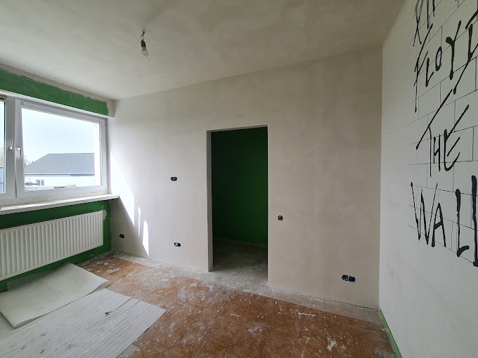 Pokój po szpachlowaniu i malowaniu, z widocznymi gładkimi ścianami, przygotowany do dalszych prac wykończeniowych. Na jednej ze ścian widnieje czarny napis 'Pink Floyd The Wall'.