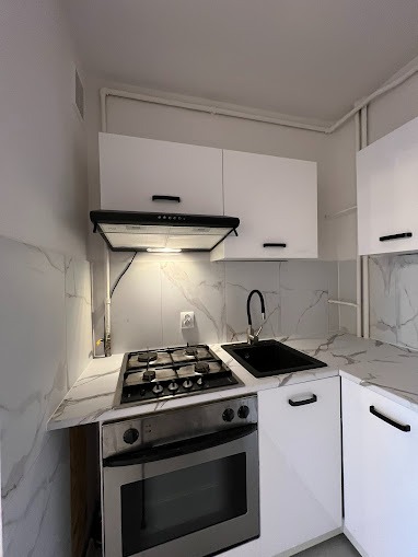 Nowoczesna, biała kuchnia z czarnymi akcentami: bateria, zlew i uchwyty, marmurowe blaty i ściany, srebrna kuchenka gazowa z piekarnikiem.