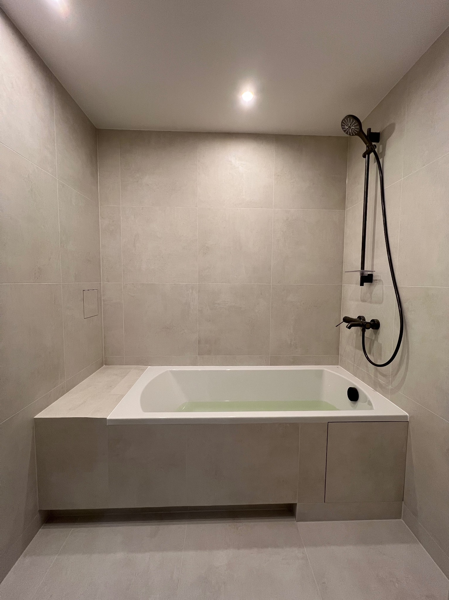 Nowoczesna łazienka po remoncie: wanna z czarną armaturą, beżowe płytki na ścianach i podłodze, minimalistyczny design. Widok na całą wannę z prysznicem.