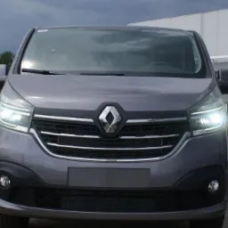 Szary Renault Trafic z włączonymi światłami mijania, zaparkowany w Wejherowie na tle budynku z napisem 'minut'.