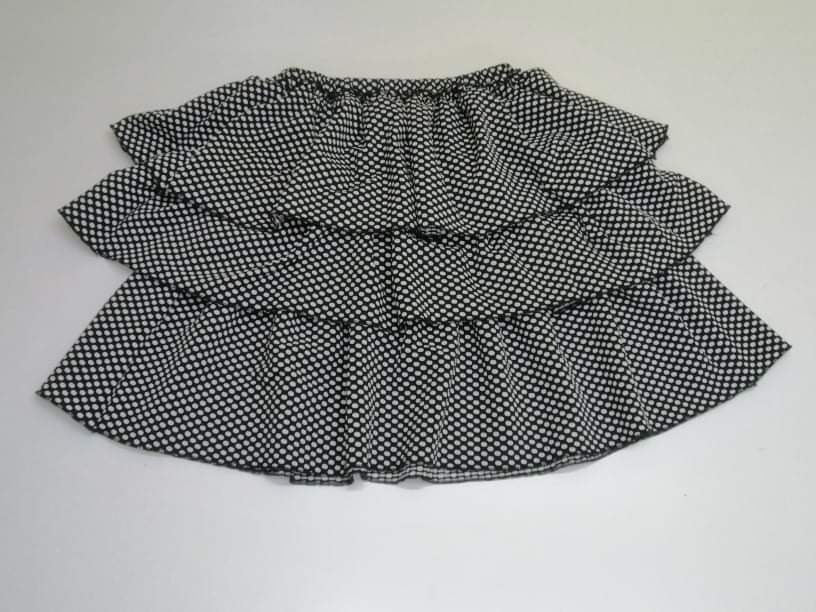 Czarno-biała, trójwarstwowa spódniczka dla dziewczynki w drobne groszki, leżąca na białym tle, z widocznym elastycznym pasem.
