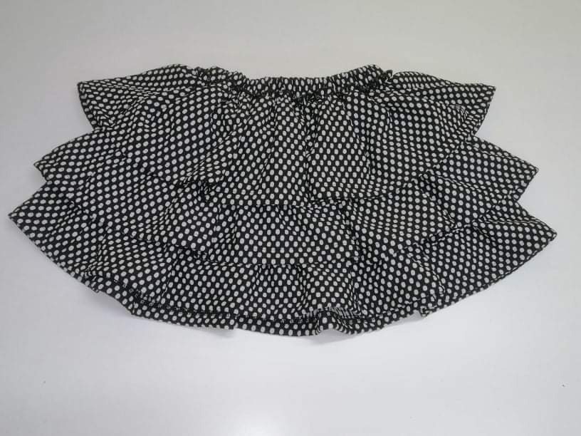 Czarno-biała, dwuwarstwowa spódniczka z falbankami w drobne kropeczki, leżąca na jasnym tle.
