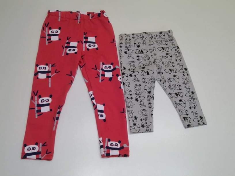 Dwie pary dziecięcych legginsów: czerwone z motywem pand na bambusach i szare z wzorem Snoopy, leżące na jasnym tle.