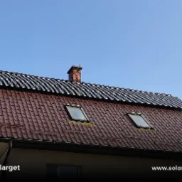 Panele fotowoltaiczne zamontowane na dachu domu z brązową dachówką i dwoma oknami dachowymi, widok z dołu w słoneczny dzień.