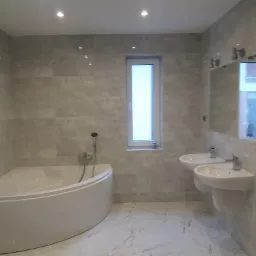 Nowoczesna łazienka z narożną wanną, dwoma umywalkami na ścianie, szarą płytką imitującą kamień i marmurową podłogą.