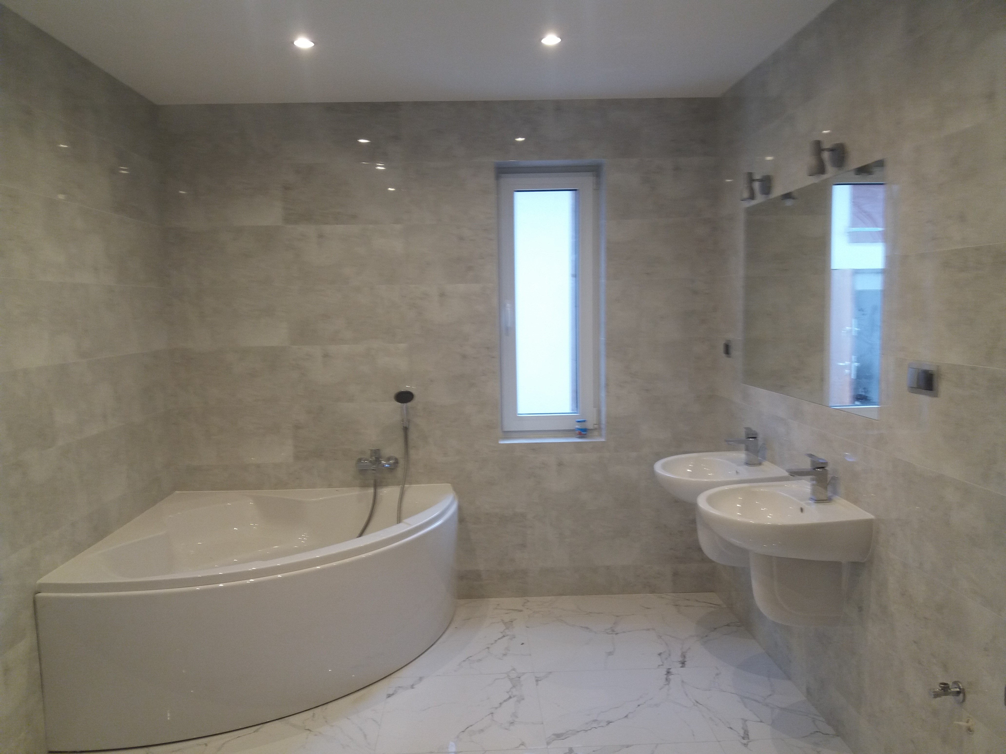 Nowoczesna łazienka z narożną wanną, dwoma umywalkami na ścianie, szarą płytką imitującą kamień i marmurową podłogą.