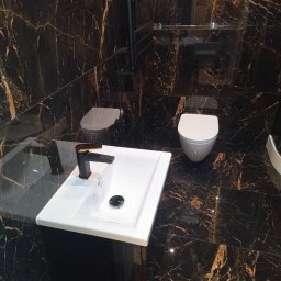 Sebastian Napierała - Wykończona łazienka z czarnymi marmurowymi płytkami, białą umywalką z czarną baterią i wiszącą toaletą.