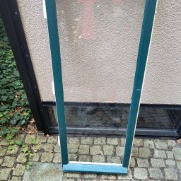 Sebastian Napierała - Pomalowana na zielono rama okienna, bez szyby, oparta o ścianę na brukowanym podłożu w Lesznie.