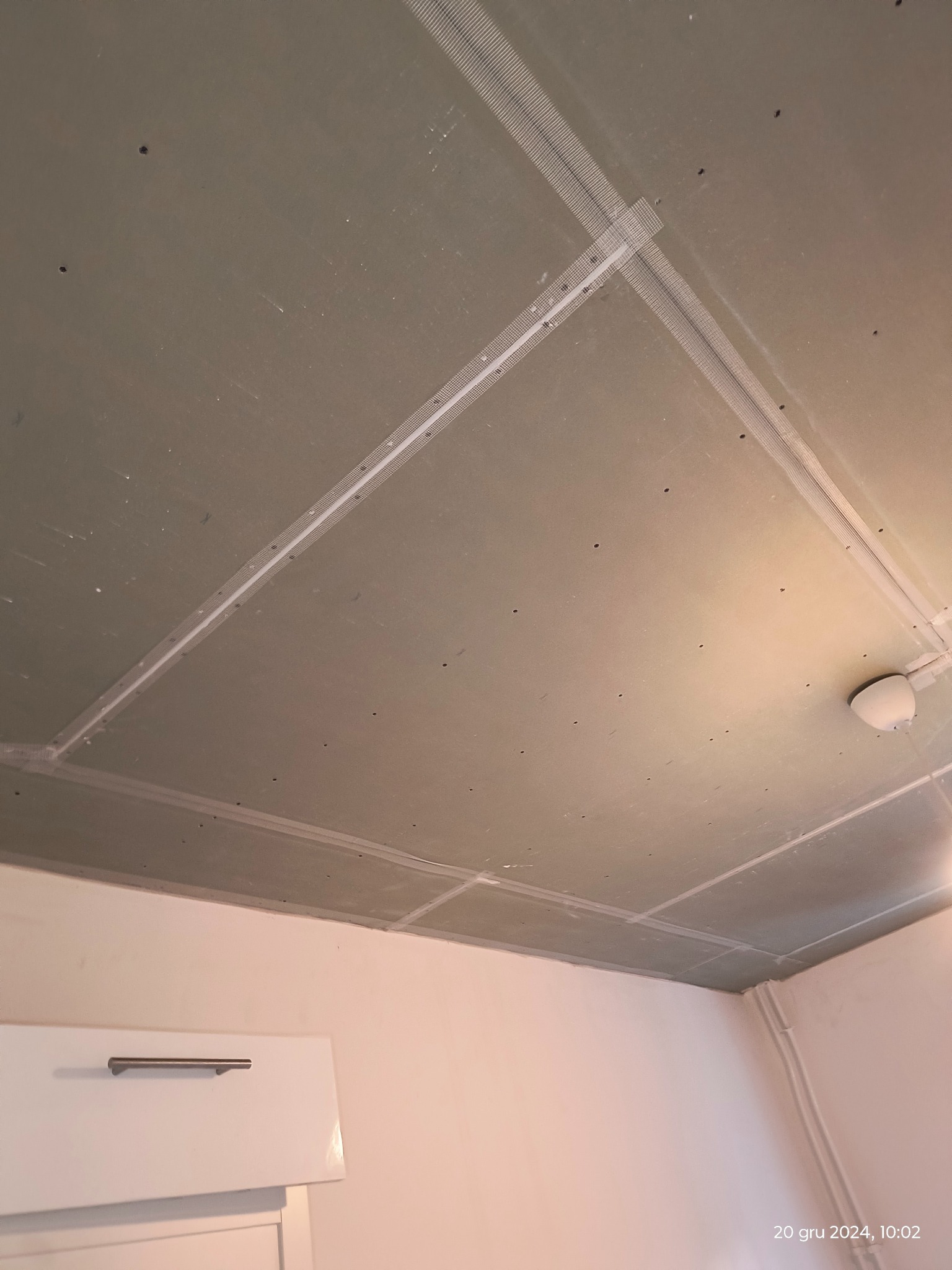 Sufit z płyt karton gips, wzmocniony siatką na łączeniach, widoczne otwory po wkrętach, przygotowany do szpachlowania i malowania.