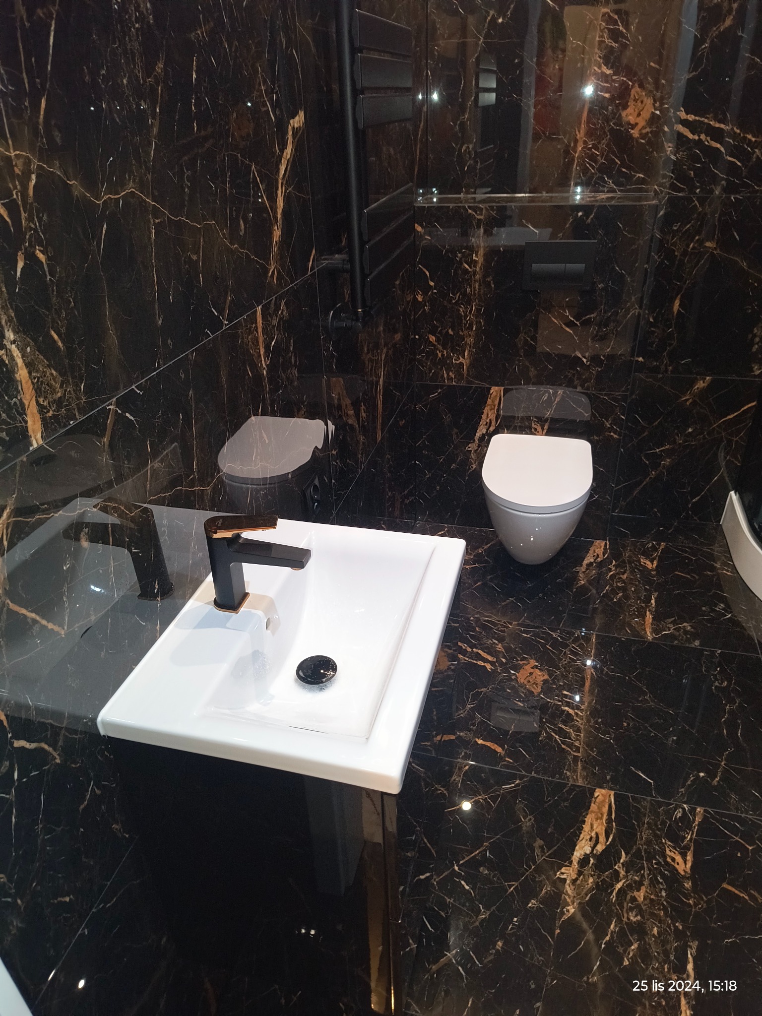Wykończona łazienka z czarnymi marmurowymi płytkami, białą umywalką z czarną baterią i wiszącą toaletą.