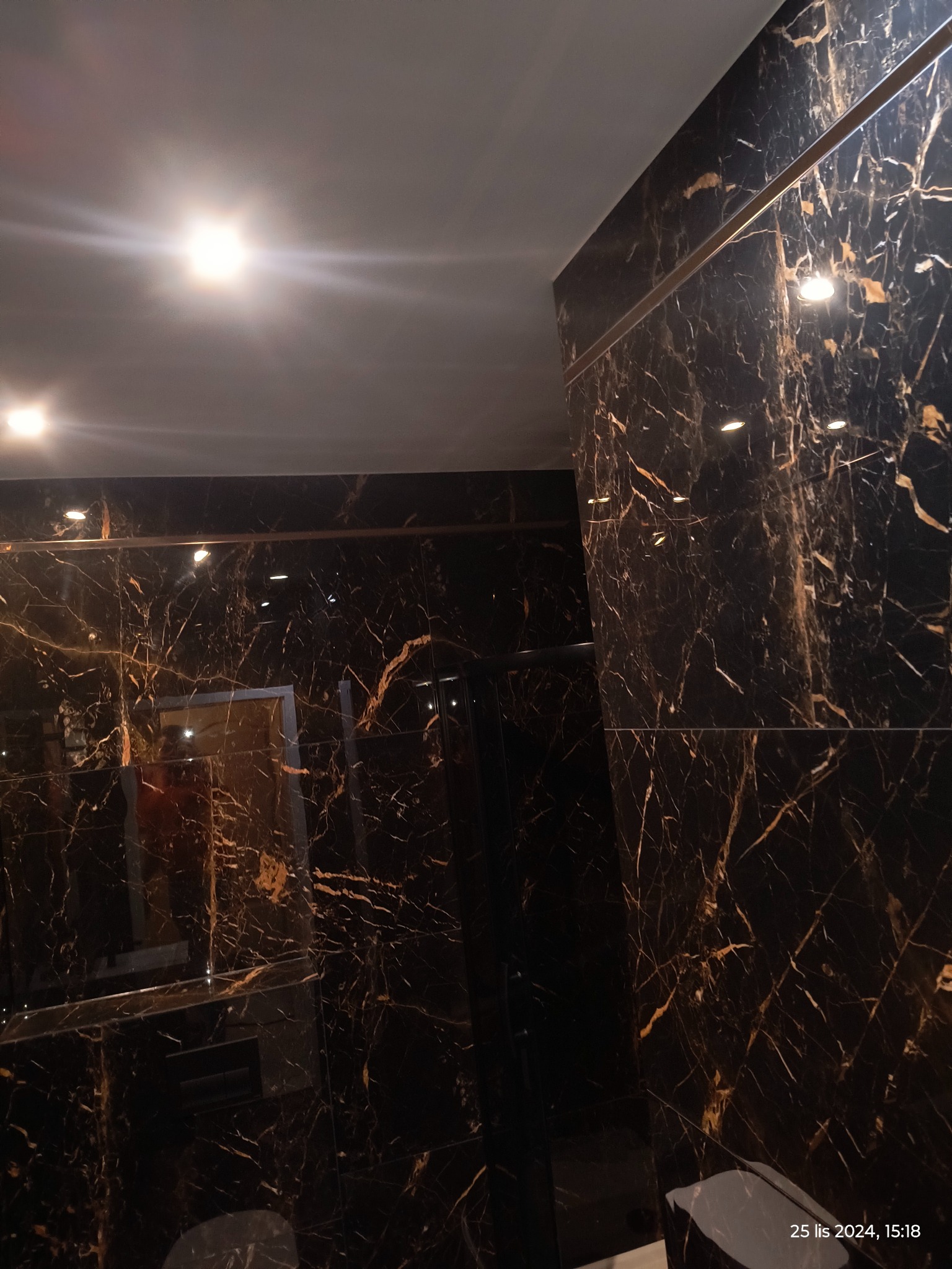 Ściany i sufit wyłożone czarnym marmurem z wyraźnym złotym użyleniem, oświetlone punktowymi lampami, tworzące luksusowe wnętrze.