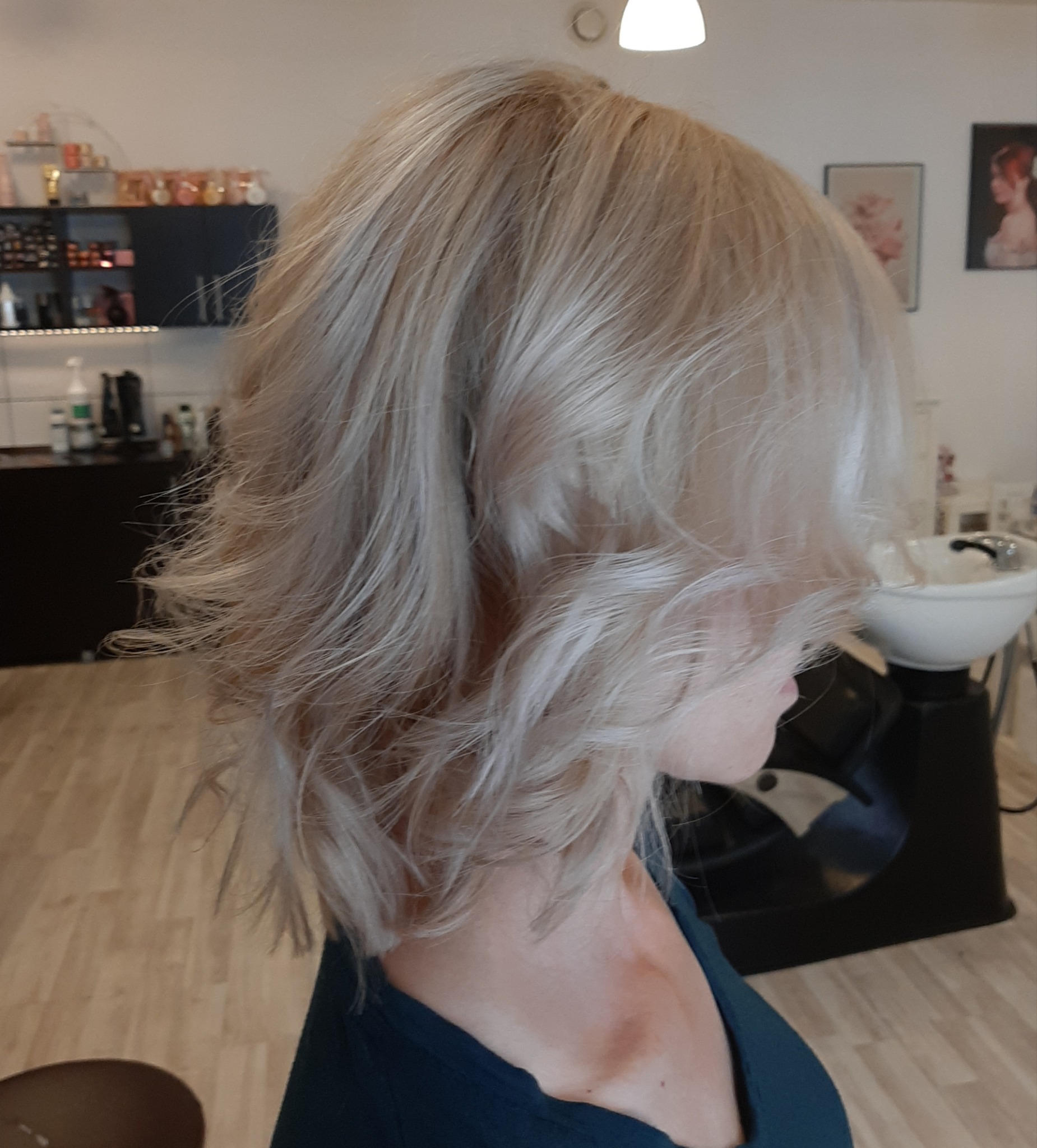 Profil kobiety z blond, pofalowanymi włosami o długości do ramion, świeżo po koloryzacji i strzyżeniu w salonie fryzjerskim.