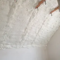 Poddasze ocieplone białą pianką poliuretanową, widoczne drewniane elementy konstrukcyjne z metalowymi łącznikami, ściany pomalowane na biało.