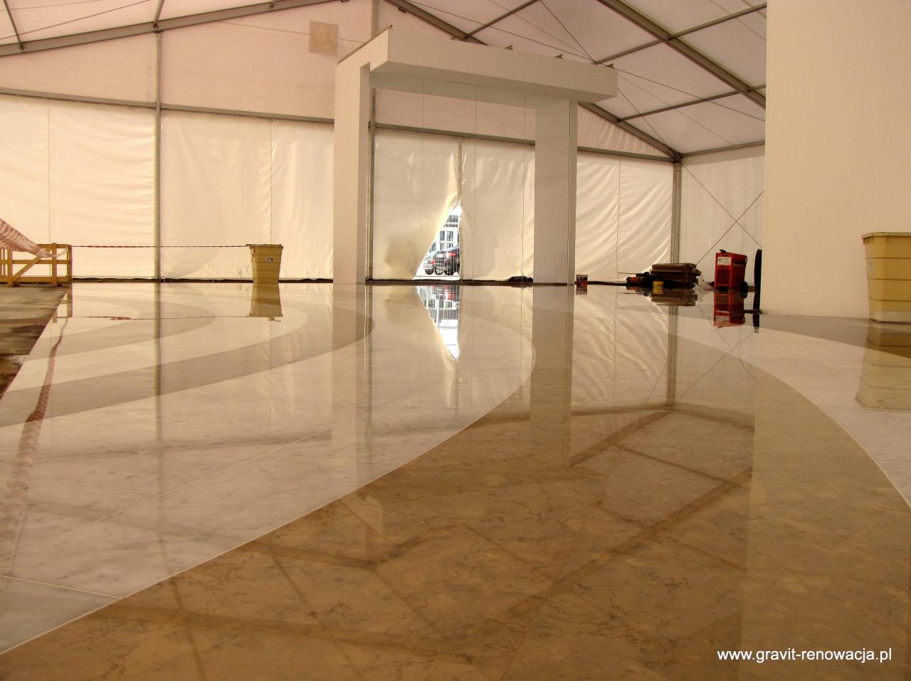 Polerowana marmurowa posadzka w hali namiotowej z widocznymi refleksami światła, narzędzia pracy w tle. Jasne, neutralne kolory i geometryczny wzór na podłodze.