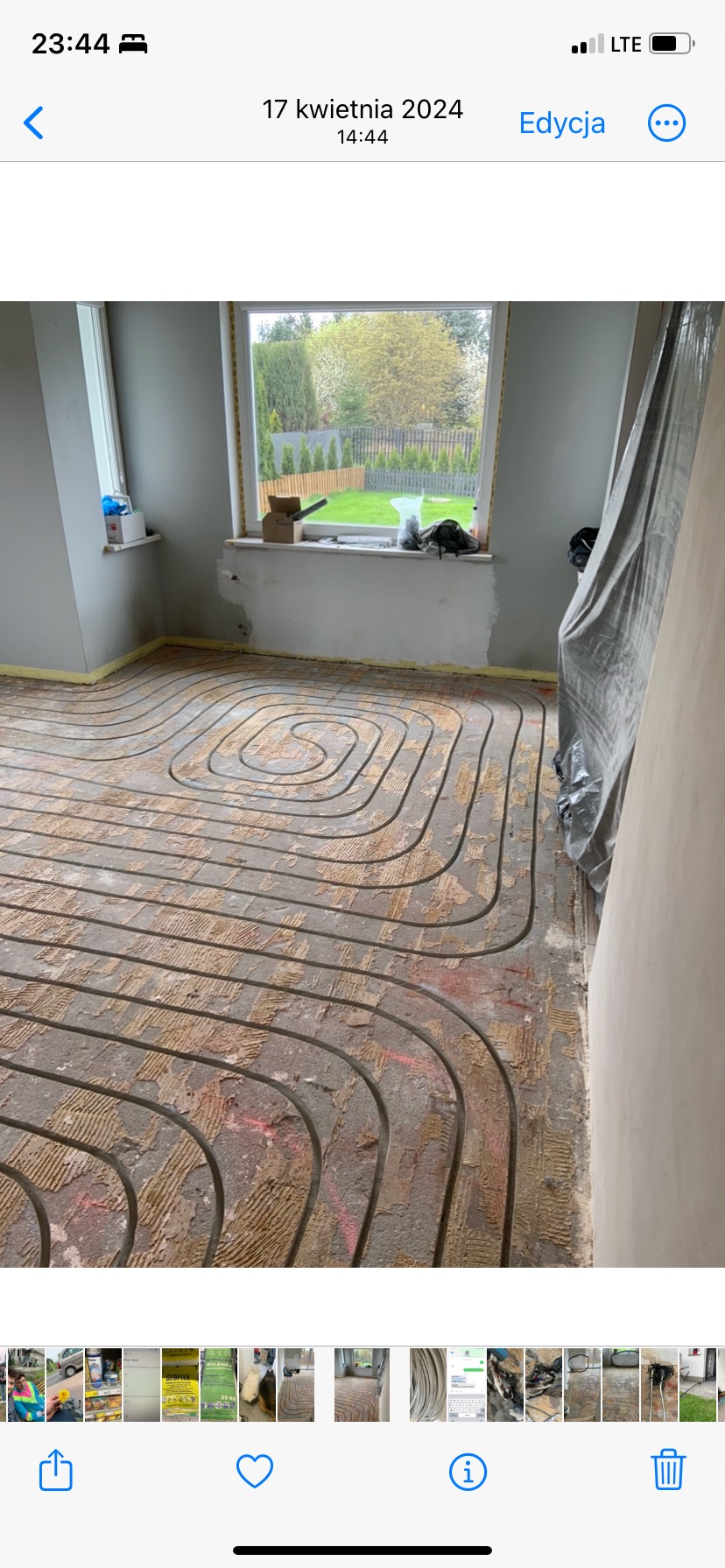 Ułożona instalacja ogrzewania podłogowego w pomieszczeniu z oknem. Widoczne rury na podłożu przed wylewką. Fragment okna z widokiem na zieleń.