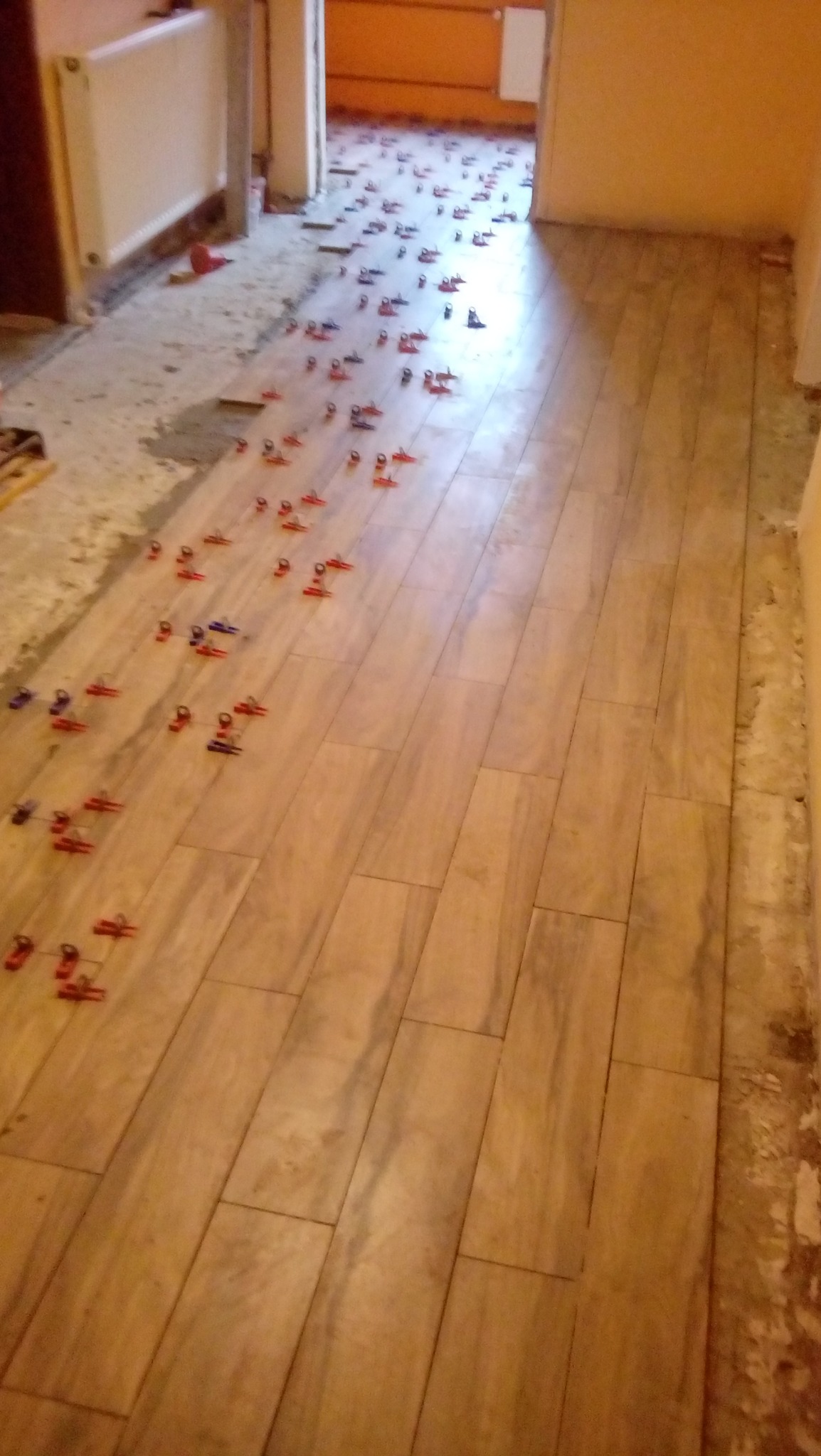 Układanie podłogi z płytek imitujących drewno; widoczne krzyżyki dystansowe w kolorach czerwonym i niebieskim, ściany przygotowane pod wykończenie.