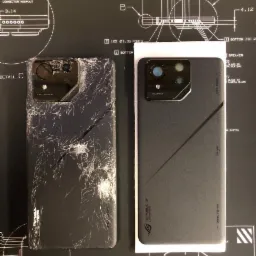 Uszkodzony smartfon ROG Phone obok nowego, na czarnym tle z technicznymi rysunkami. Ekran i tylna obudowa starego telefonu są całkowicie popękane, ukazując stopień uszkodzenia.