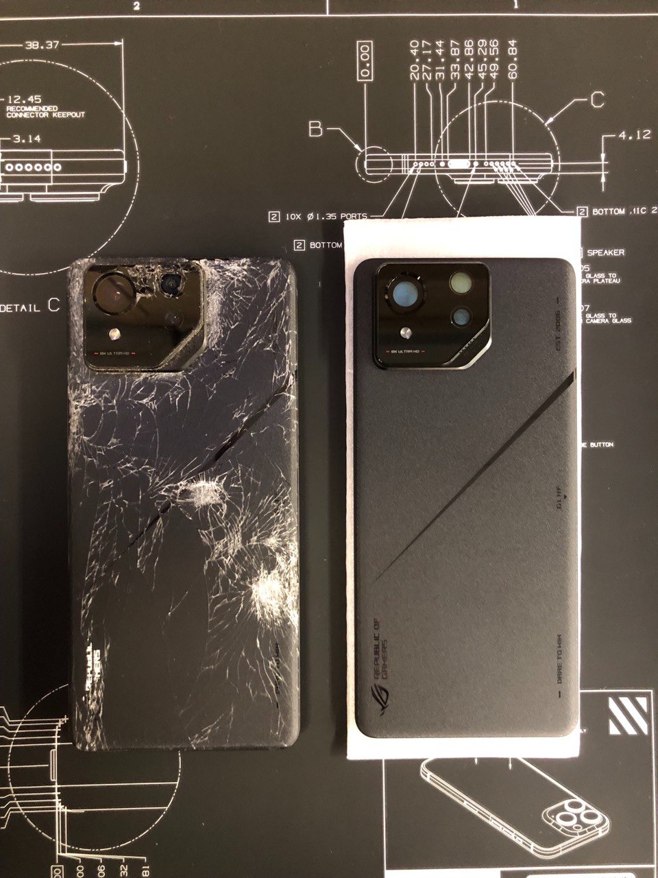 Uszkodzony smartfon ROG Phone obok nowego, na czarnym tle z technicznymi rysunkami. Ekran i tylna obudowa starego telefonu są całkowicie popękane, ukazując stopień uszkodzenia.