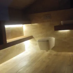 Nowoczesna łazienka z podświetleniem LED pod półkami i toaletą podwieszaną, wykończona płytkami w odcieniach beżu i brązu, z drewnianymi elementami wyposażenia.