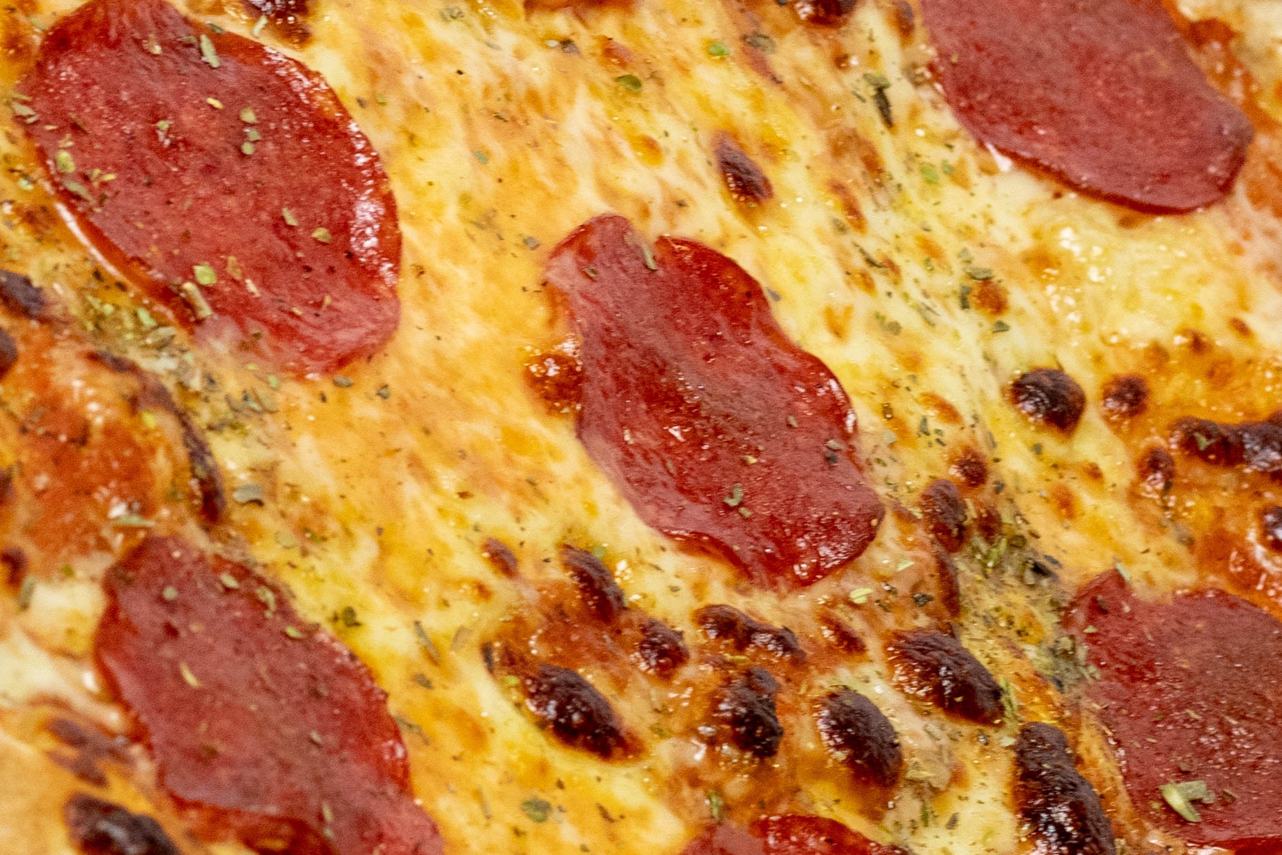 Zbliżenie na pizzę pepperoni z wyraźnie widocznymi przyprawami i stopionym serem z delikatnymi przypaleniami.