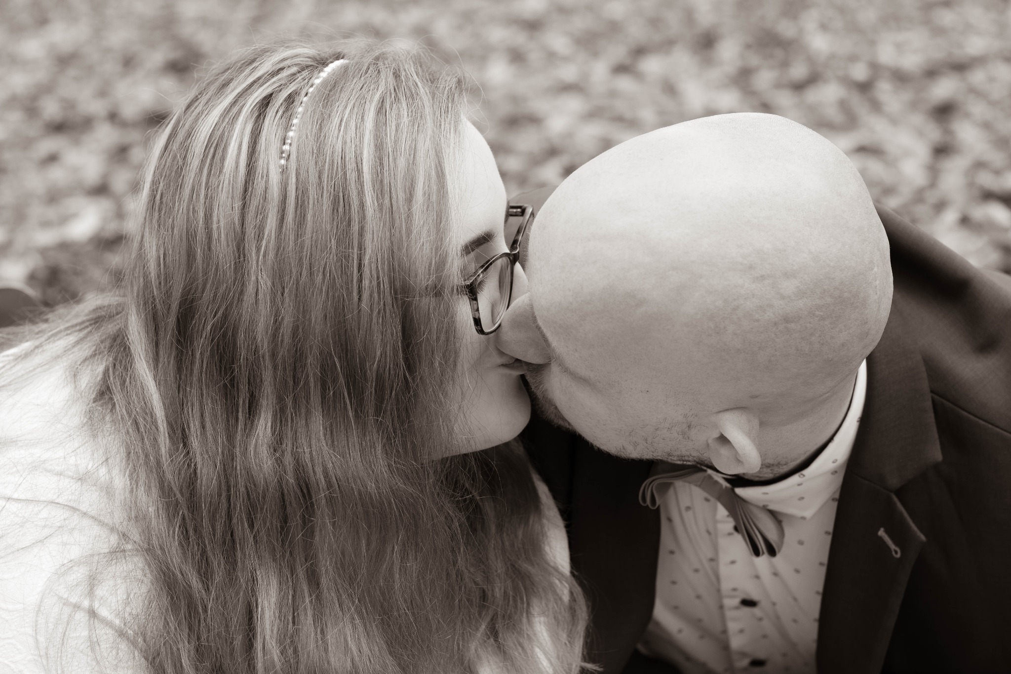 Sepia zdjęcie pary całującej się, kobieta w okularach i z perłową ozdobą we włosach, mężczyzna w garniturze z muszką.