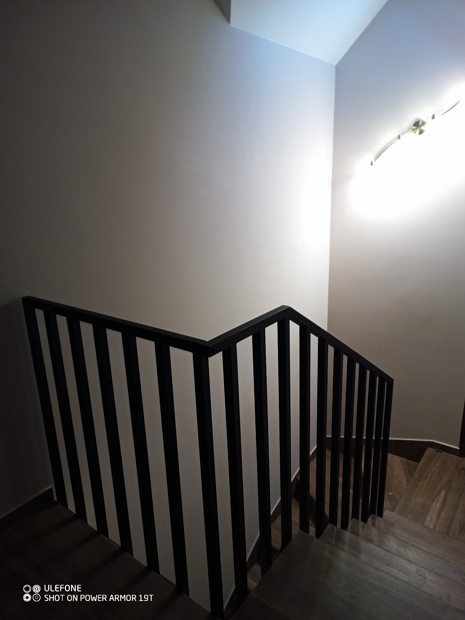 Minimalistyczne schody z czarną metalową balustradą w nowoczesnym wnętrzu. Ujęcie z góry, podkreślające geometrię i kontrast bieli ścian z ciemnym drewnem.