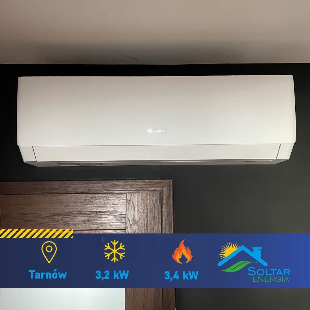 Biały klimatyzator Gree zamontowany na ciemnej ścianie nad drewnianymi drzwiami. Na dole grafika z parametrami urządzenia i logo Soltar Energia.