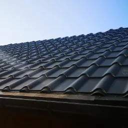 Nowy, czarny dach z dachówki ceramicznej, widok z dołu pod kątem, fragment rynny i nieba w tle.